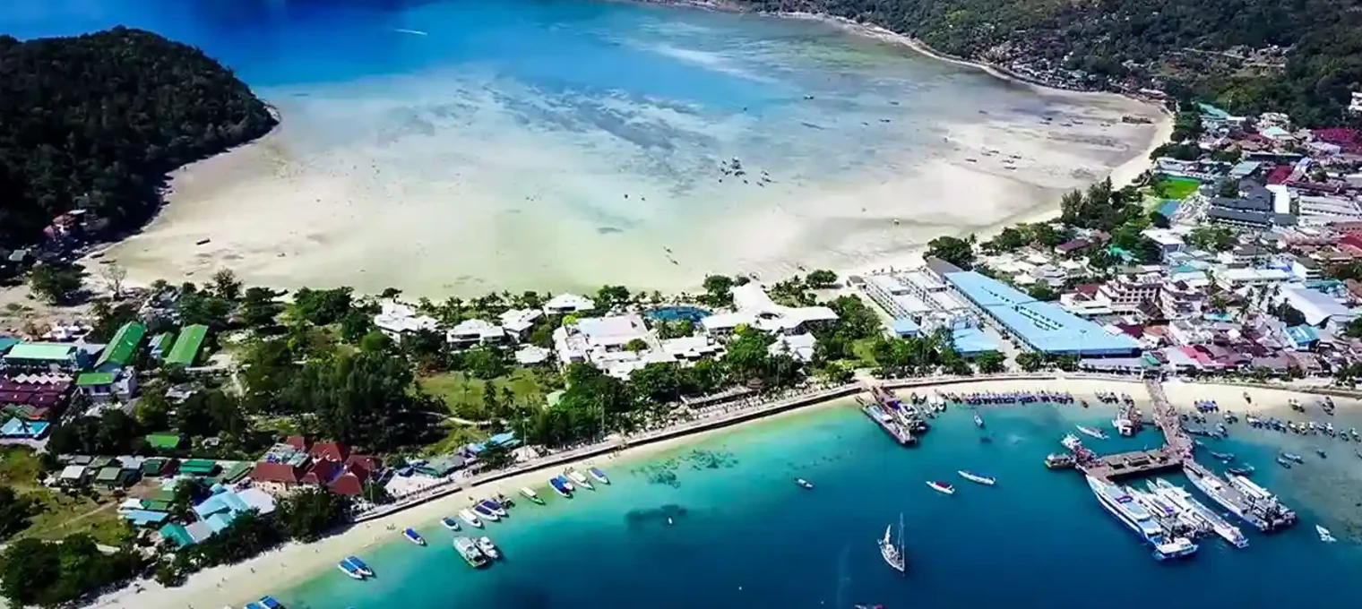 Aerial view of Phuket's coastline with boats, beach, and lush green mountains.