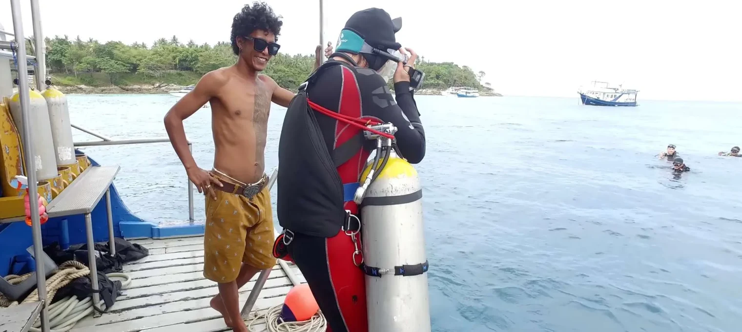 Diver prepares to dive while another person smiles on the boat in Phuket. Sunny day at sea.