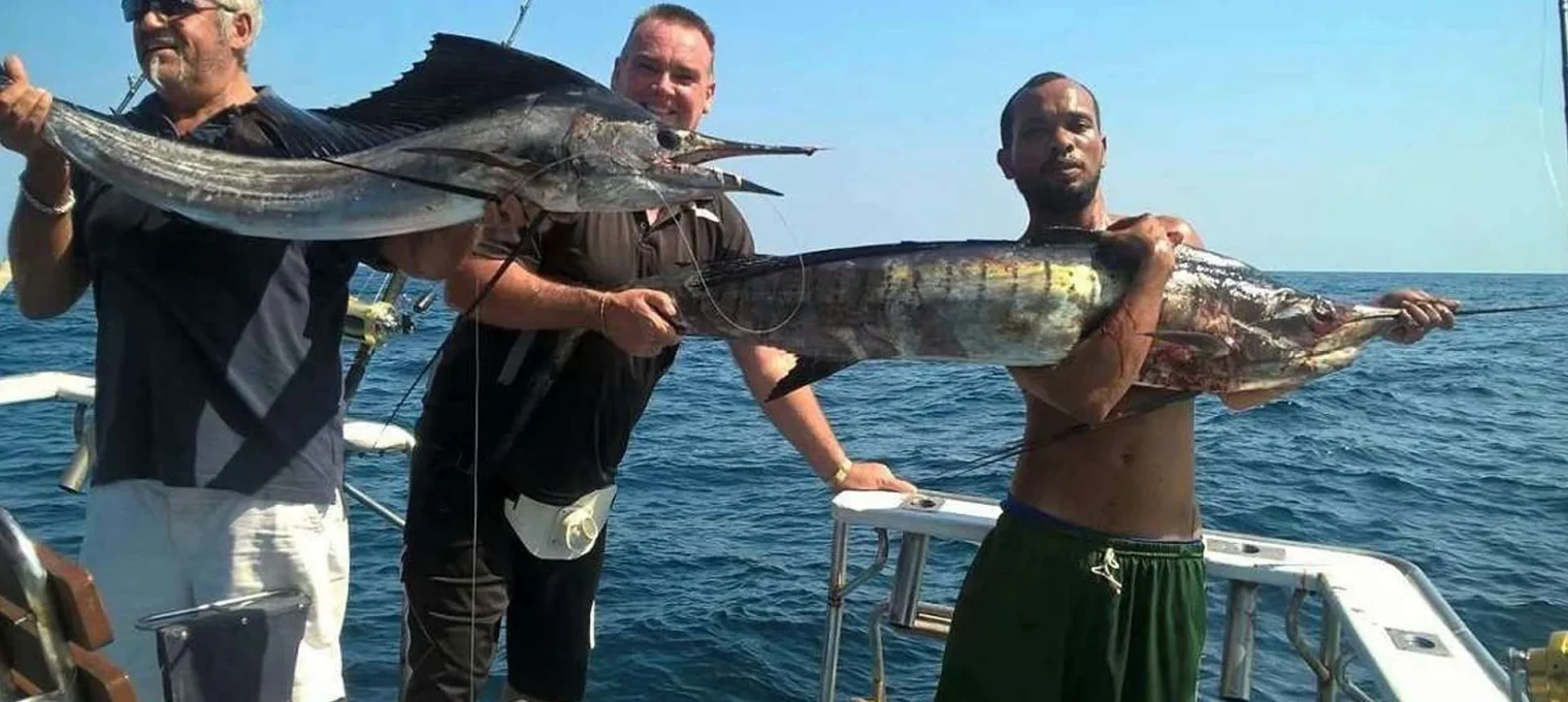 Three men proudly holding large fish on a boat in Phuket's clear blue waters.
