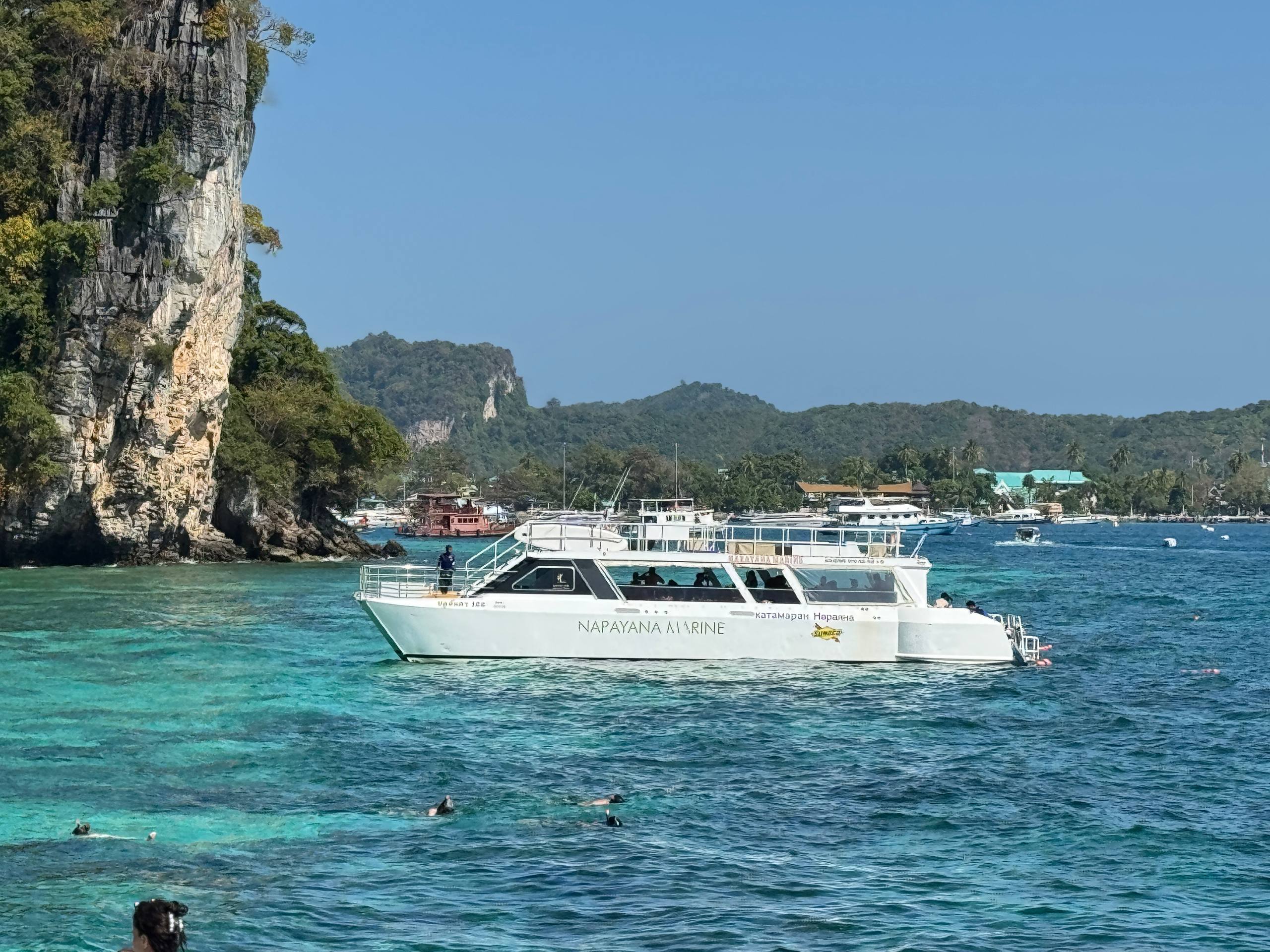 White boat cruising in the turquoise waters of Phuket, surrounded by green hills and islands.