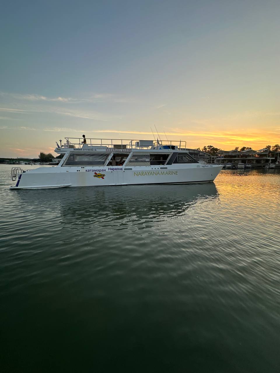 Sunset view of a white boat named Narayana Marine docking at a calm Phuket harbor.