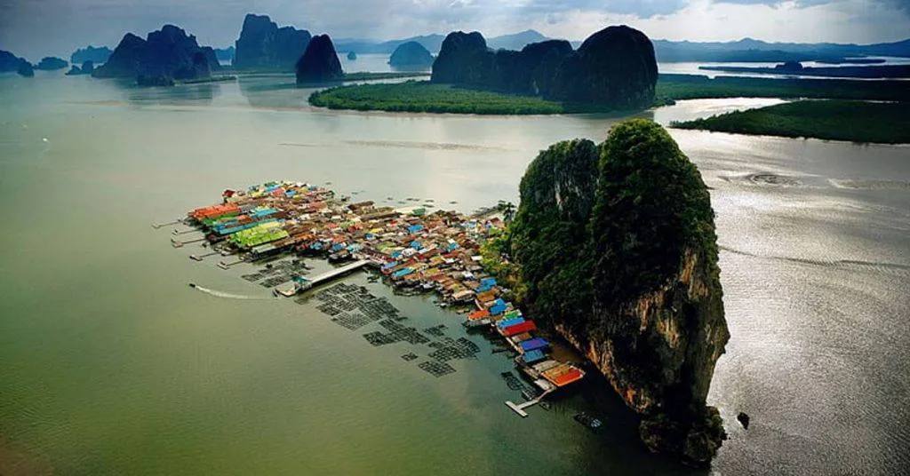 Aerial view of colorful stilt houses on water in Phuket, surrounded by towering limestone cliffs.