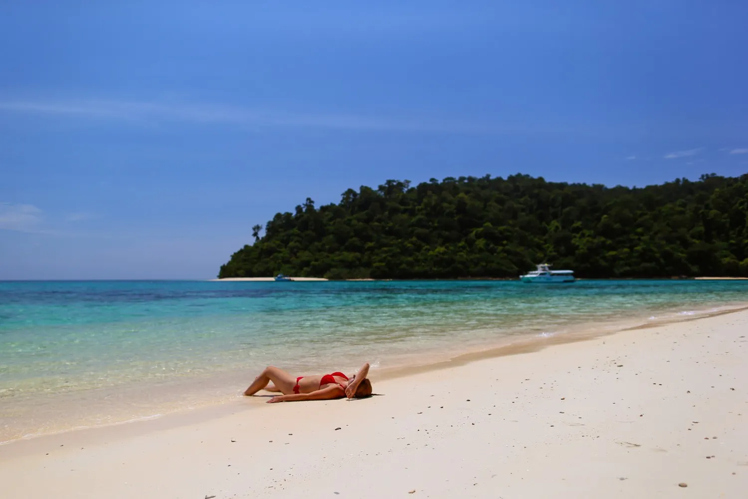 A woman in a red bikini relaxes on a sandy beach in Phuket.
