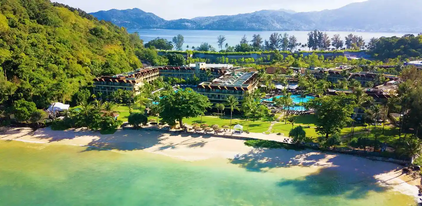 Красивая панорама курорта на пляже в Пхукете с зелеными лужайками и горами на фоне.