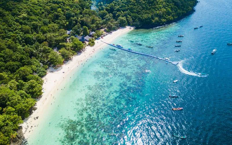 Пляж на Пхукете с белым песком, зелеными деревьями и лодками в воде.