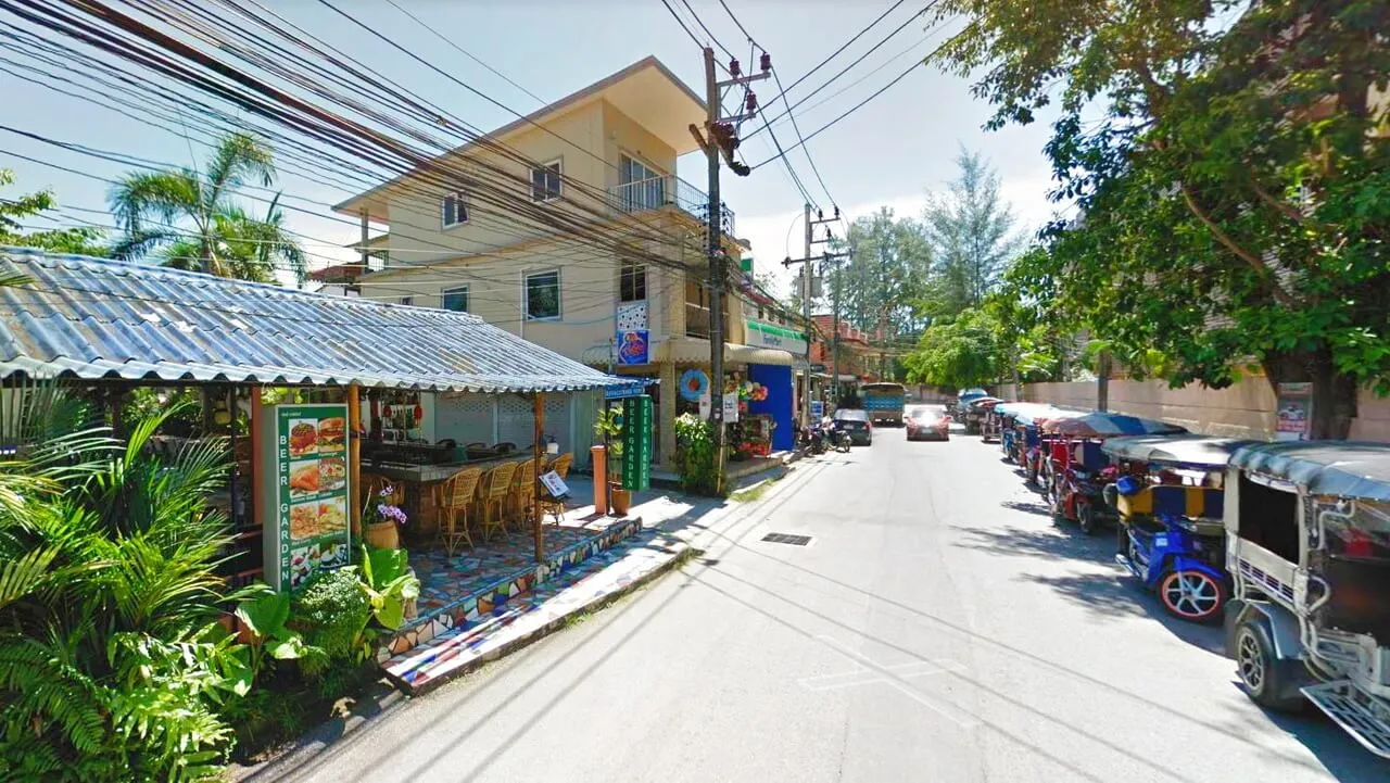 Scenic street view in Phuket with shops, eateries, and parked tuk-tuks.