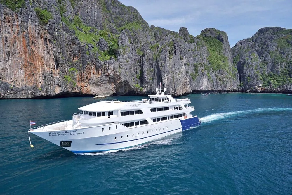 Luxury cruise ship sailing in turquoise waters near rocky cliffs in Phuket, Thailand.