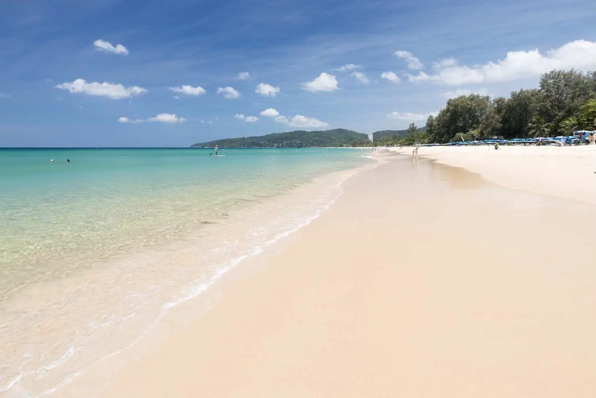 Serene beach in Phuket with clear water, soft sand, and a few people enjoying the sun.