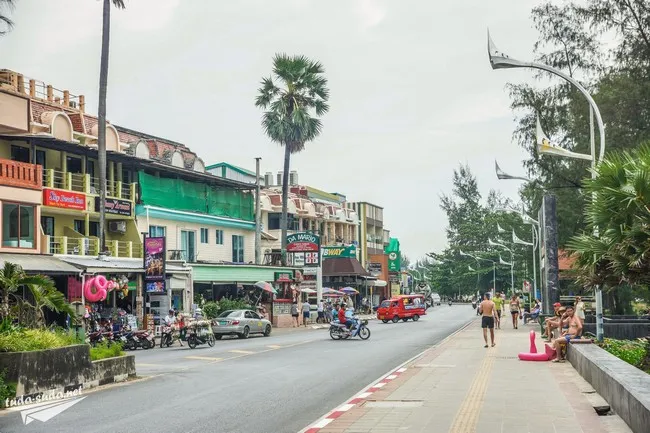 Phuket street scene with shops, palm trees, and people enjoying the outdoors.