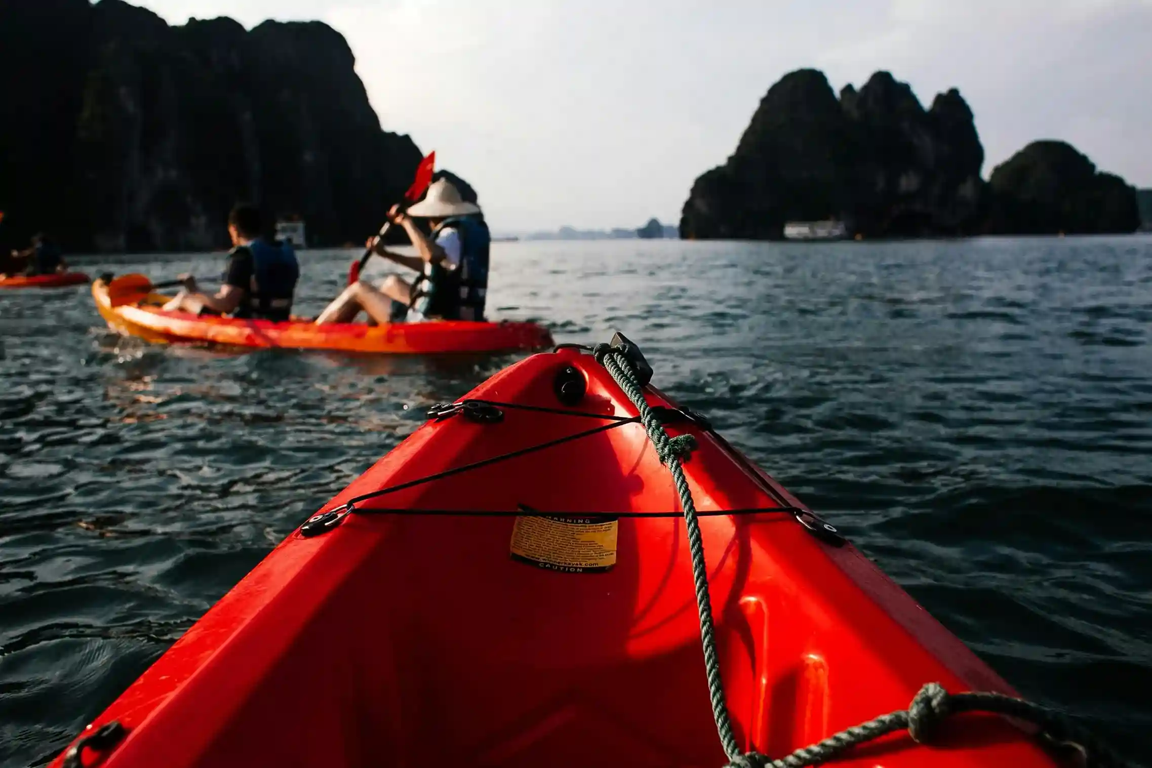 Kayakers paddle through the calm waters of Phuket with rocky cliffs in the background.
