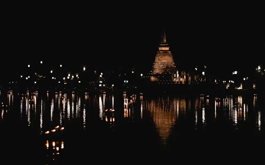 Night view of a temple in Phuket, with reflections on the water and lights in the background.