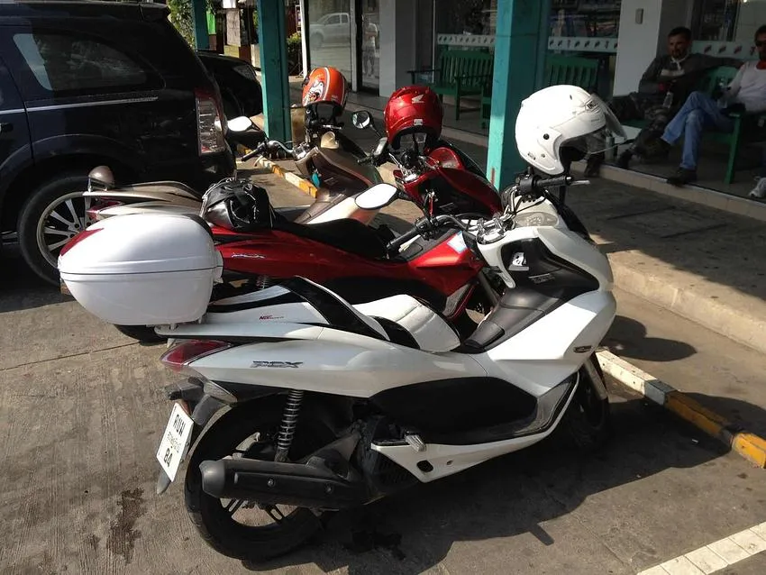 Three parked scooters with helmets outside a shop in Phuket, Thailand.