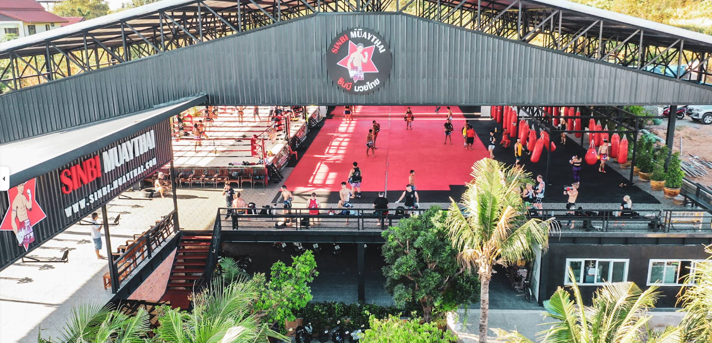 Muay Thai training facility in Phuket with outdoor ring, fighters, and tropical greenery.