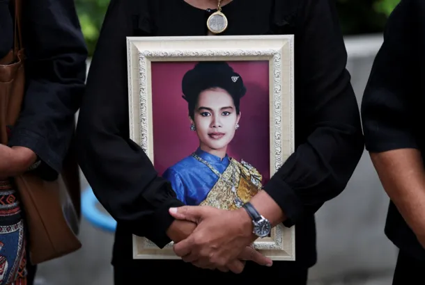 A person holds a portrait of a woman in traditional Thai attire during a memorial in Phuket.