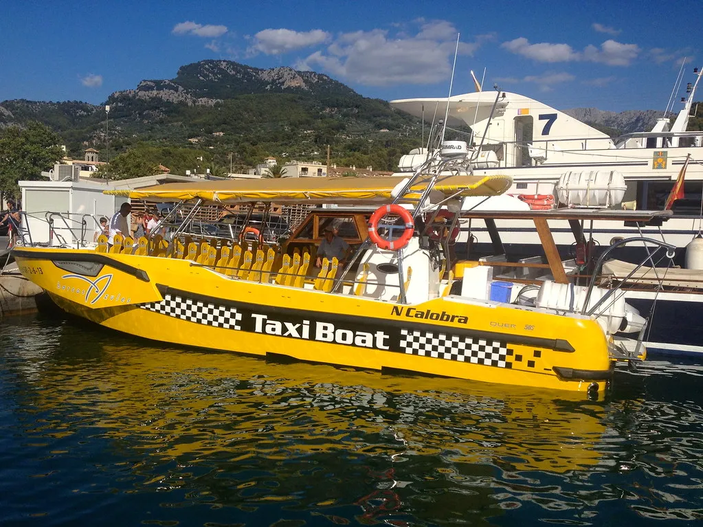 Yellow taxi boat docked in Phuket with seating for passengers and scenic mountains in background.