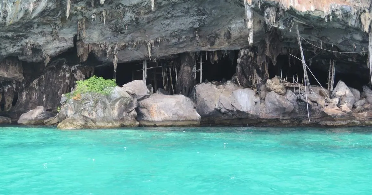 Cave entrance by the turquoise water in Phuket, surrounded by rocky cliffs.