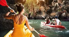 A woman paddles a kayak in Phuket, with two others kayaking nearby in the scenic waters.