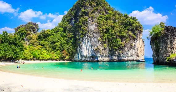 Tropical beach in Phuket with clear turquoise water, rocky cliffs, and lush greenery.
