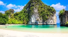 Tropical beach in Phuket with clear turquoise water, rocky cliffs, and lush greenery.