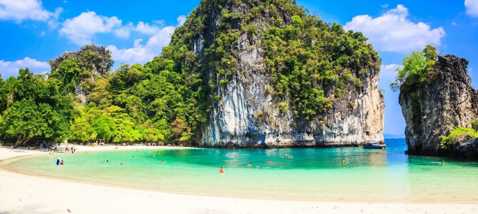 Tropical beach in Phuket with clear turquoise water, rocky cliffs, and lush greenery.