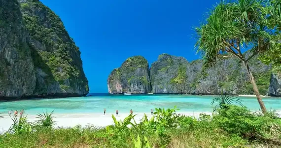 Tropical beach in Phuket with cliffs and clear turquoise waters on a sunny day.