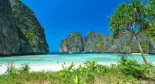 Tropical beach in Phuket with cliffs and clear turquoise waters on a sunny day.