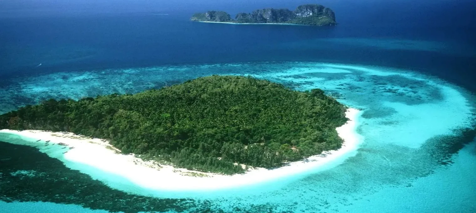 Aerial view of a tropical island in Phuket, surrounded by turquoise waters and lush greenery.