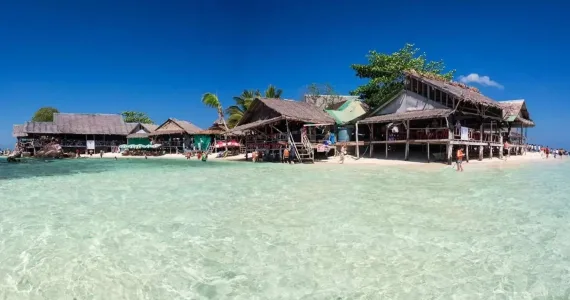 Scenic beachfront view of wooden huts in Phuket, clear turquoise water, and blue skies.