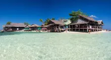 Scenic beachfront view of wooden huts in Phuket, clear turquoise water, and blue skies.