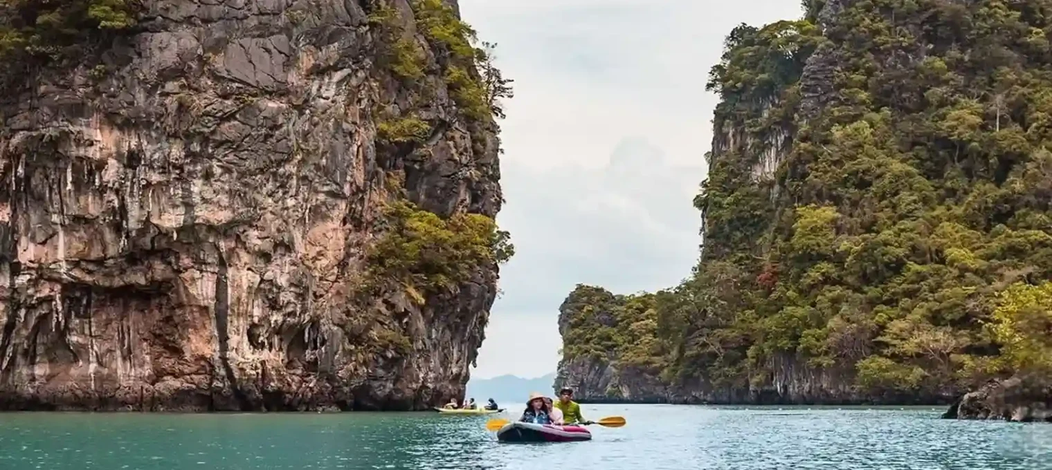 Kayakers explore the turquoise waters surrounded by dense cliffs in Phuket, Thailand.