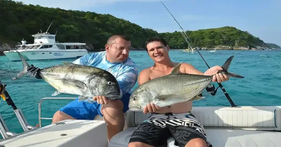 Two men proudly hold large fish while fishing in Phuket's turquoise waters.