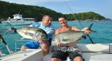 Two men proudly hold large fish while fishing in Phuket's turquoise waters.