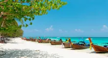 Traditional longtail boats lined on a sunny beach in Phuket, with vibrant turquoise waters.