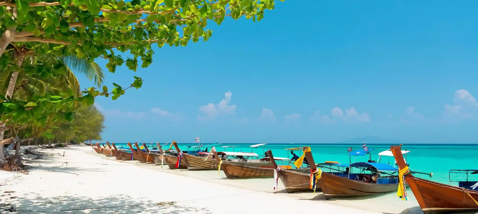 Traditional longtail boats lined on a sunny beach in Phuket, with vibrant turquoise waters.