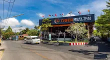 Tiger Muay Thai gym in Phuket with a blue sky and street view, surrounded by greenery.