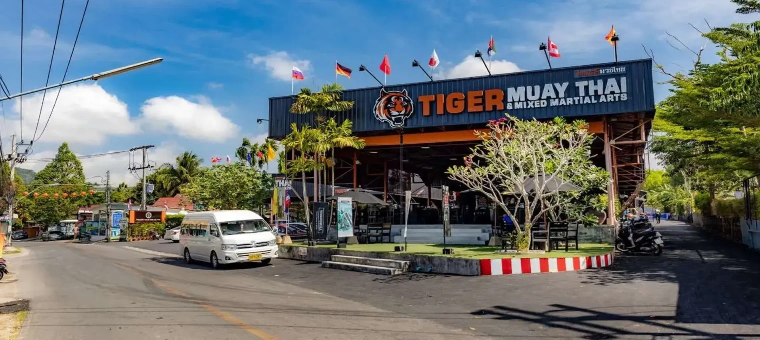 Tiger Muay Thai gym in Phuket with a blue sky and street view, surrounded by greenery.