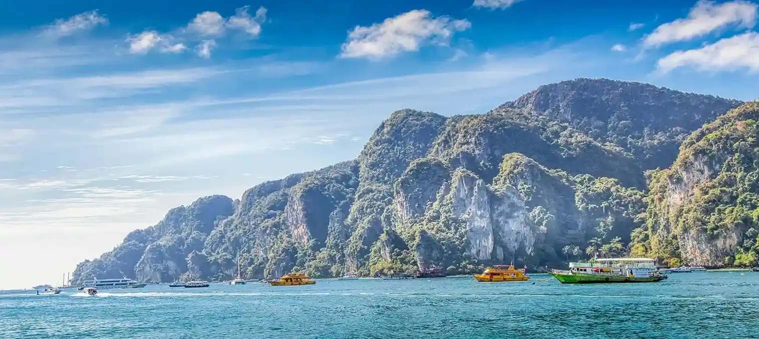 Stunning view of boats near rocky cliffs and turquoise waters in Phuket, Thailand.