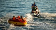 A person riding a jet ski pulls a group on a colorful inflatable raft in Phuket waters.