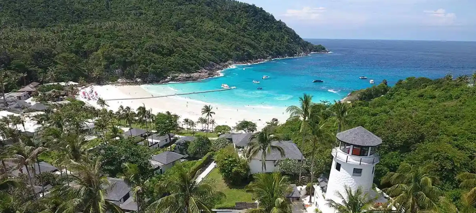 Aerial view of a lighthouse on a beach in Phuket with turquoise waters and lush greenery.