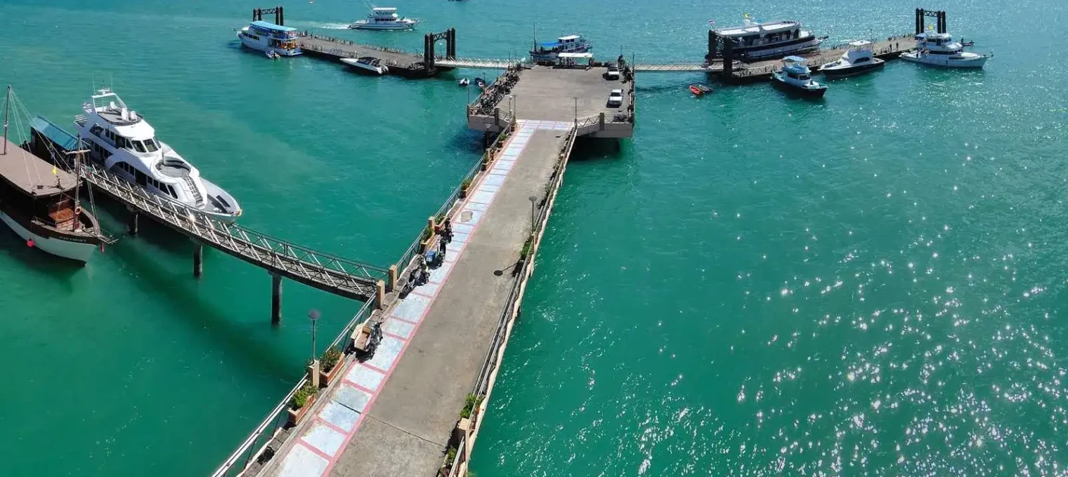 Pier with boats docked in clear turquoise waters of Phuket, Thailand.