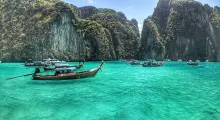 Traditional boats on turquoise waters in Phuket, surrounded by lush cliffs and nature.