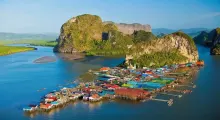 Colorful stilt houses in a bay surrounded by lush green hills in Phuket, Thailand.