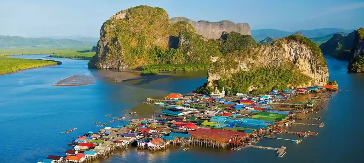 Colorful stilt houses in a bay surrounded by lush green hills in Phuket, Thailand.
