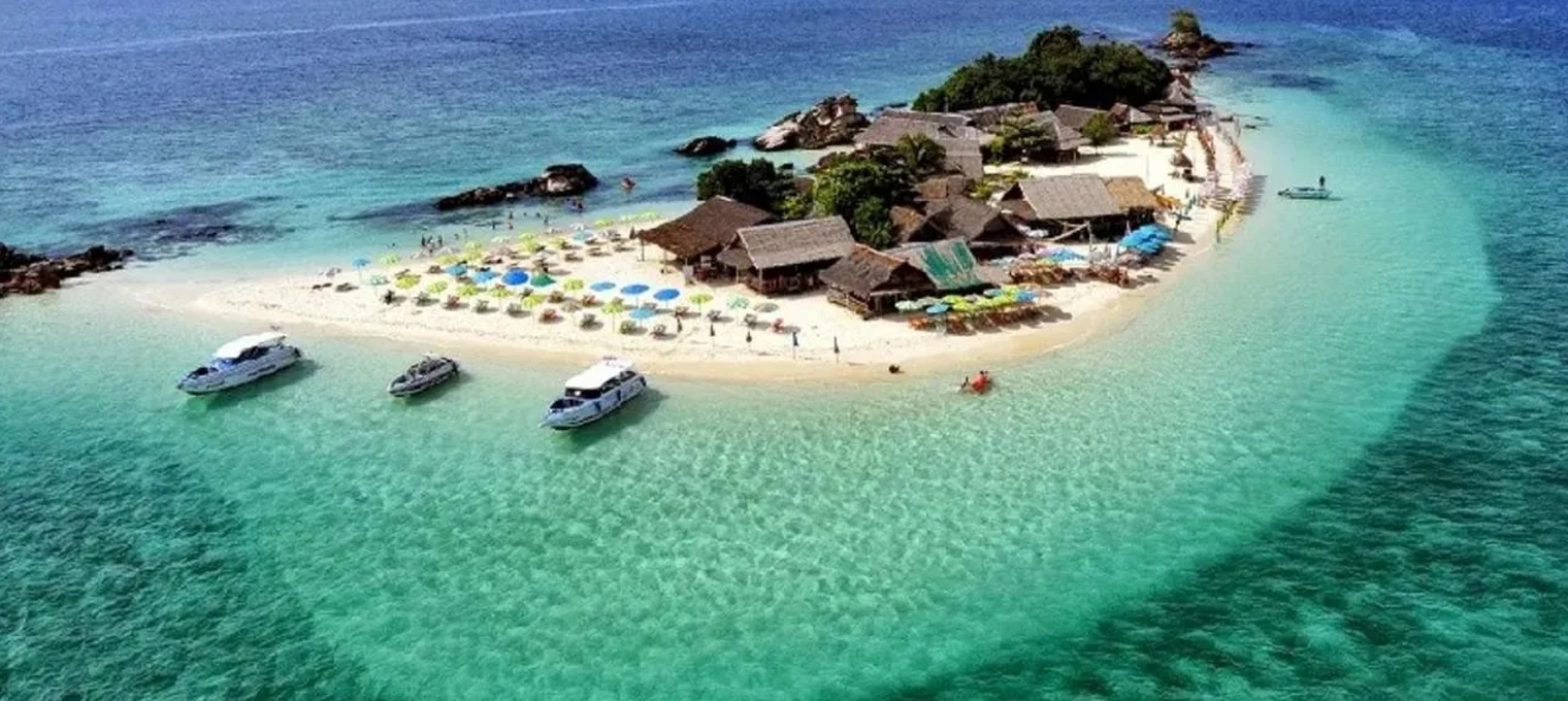 Aerial view of a tropical island in Phuket with clear blue water and beach umbrellas.