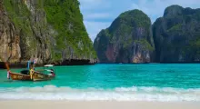 Scenic view of turquoise waters, a longtail boat, and limestone cliffs in Phuket.