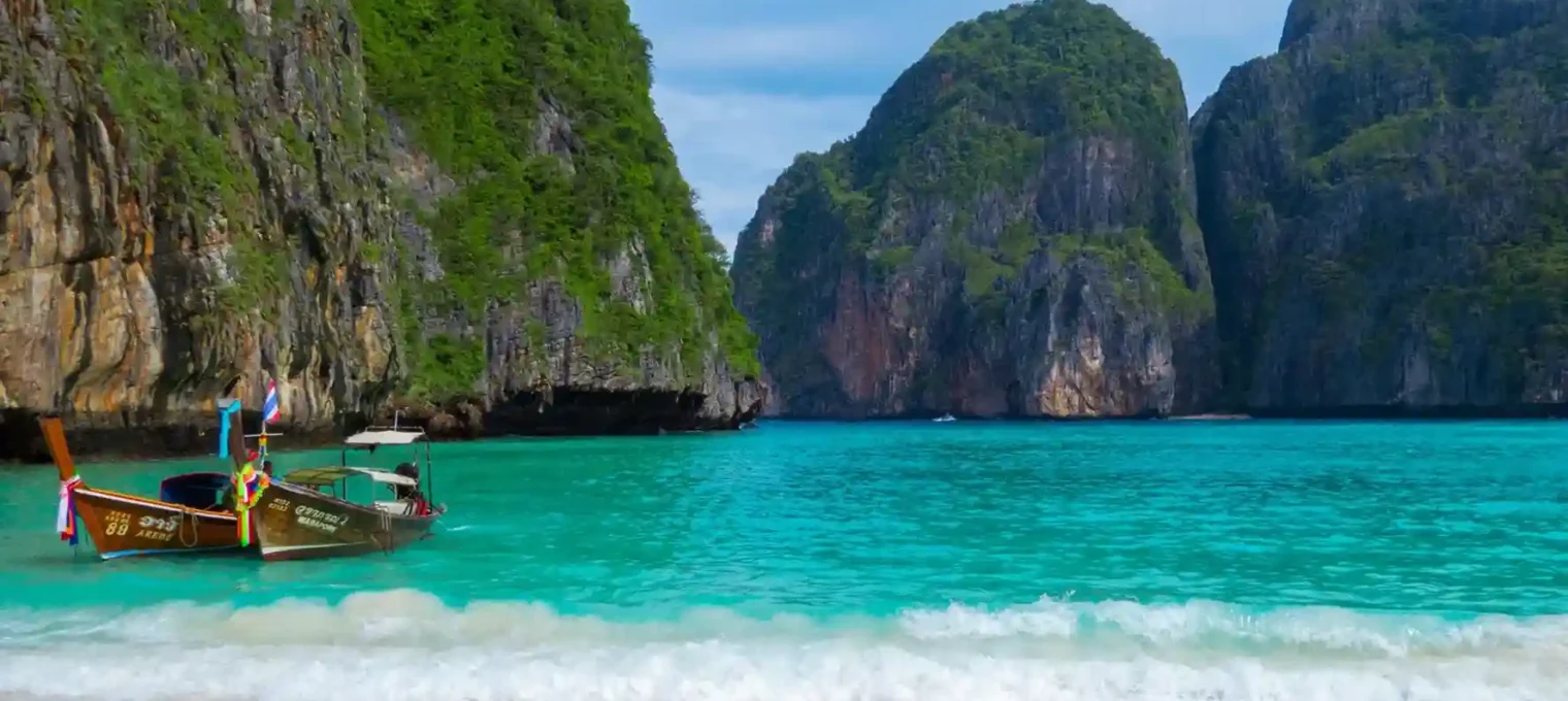 Scenic view of turquoise waters, a longtail boat, and limestone cliffs in Phuket.