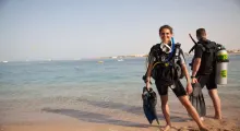 Two divers in wetsuits stand on a beach in Phuket, ready for an underwater adventure.