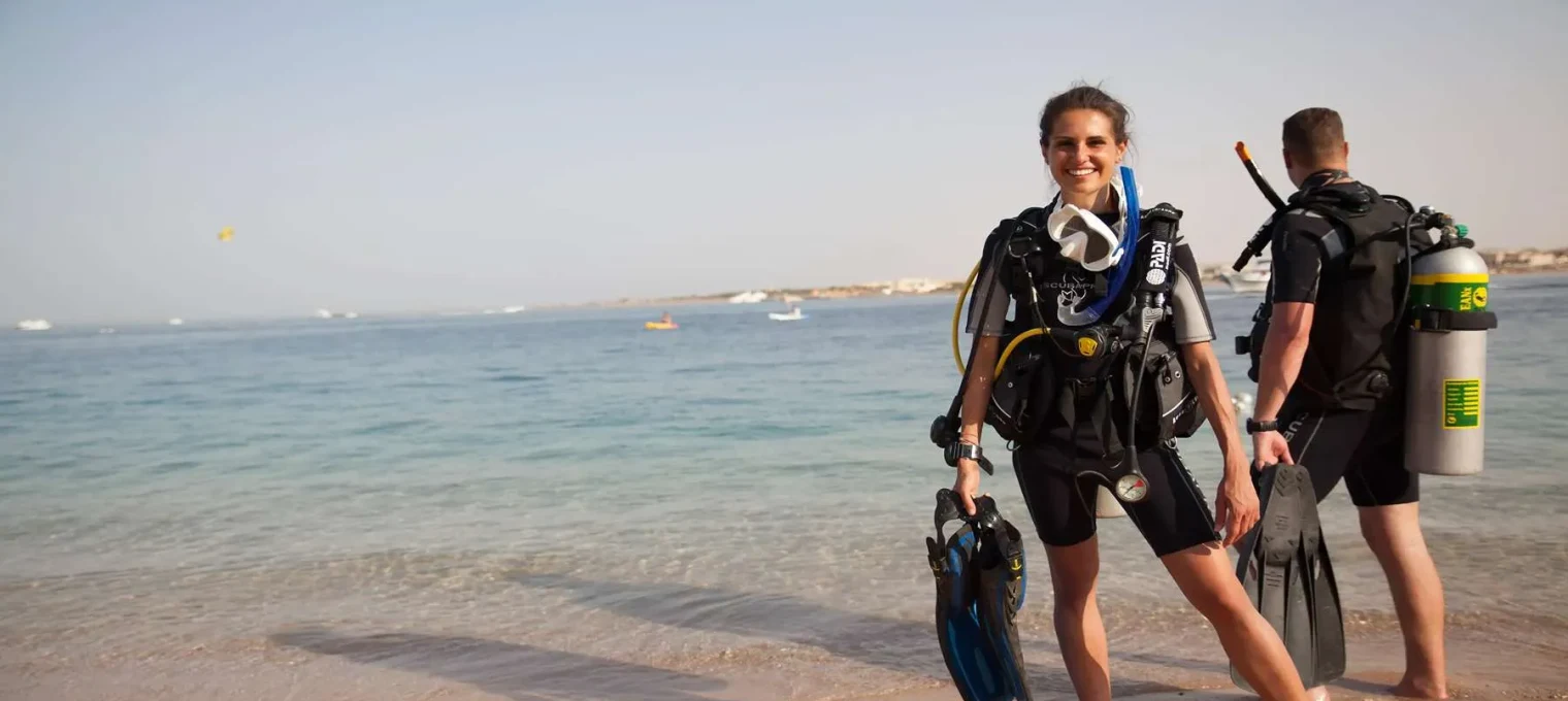 Two divers in wetsuits stand on a beach in Phuket, ready for an underwater adventure.