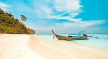 A long-tail boat anchored on a sandy beach in Phuket, surrounded by turquoise waters.