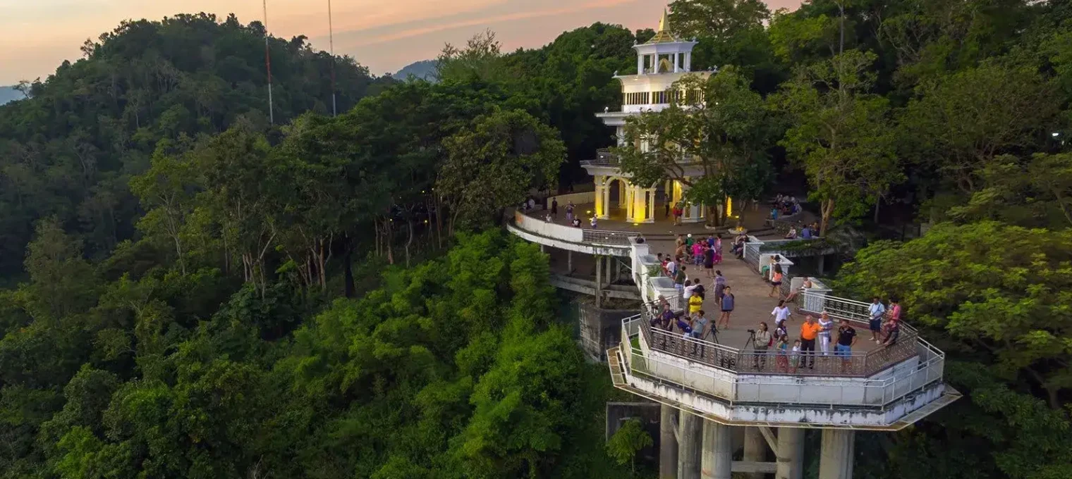Смотровая площадка на холме в Пхукете с туристами на фоне заката и зелени.